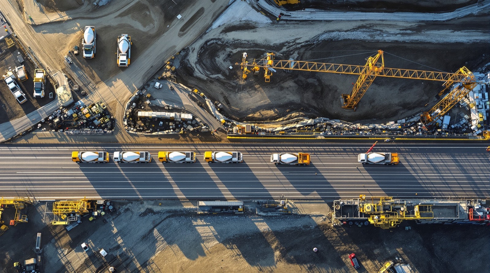 Mixer trucks queued along a haul road beside a construction site at first light